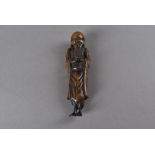 A Japanese wood carved netsuke, modelled as a standing Sennin, with hands clasped together at