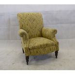 An Edwardian upholstered armchair, with turned front supports and ceramic castors with floral and