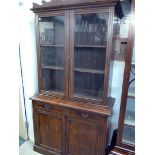 A mahogany stained bookcase display, with two glazed doors above single drawer and lower cupboard
