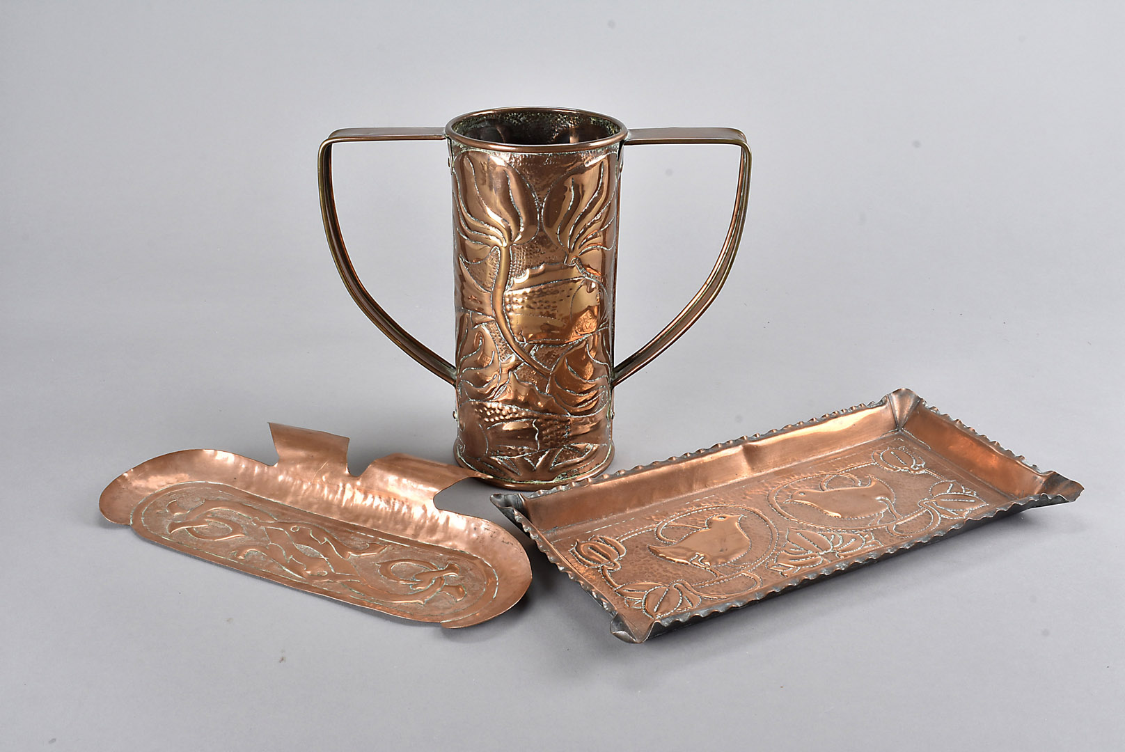 An arts and crafts Newlyn style copper twin handled vase, with hammer beaten design of fish swimming