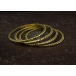 A set of four high carat gold Indian bangles, with raised niello style pattern design to outer,