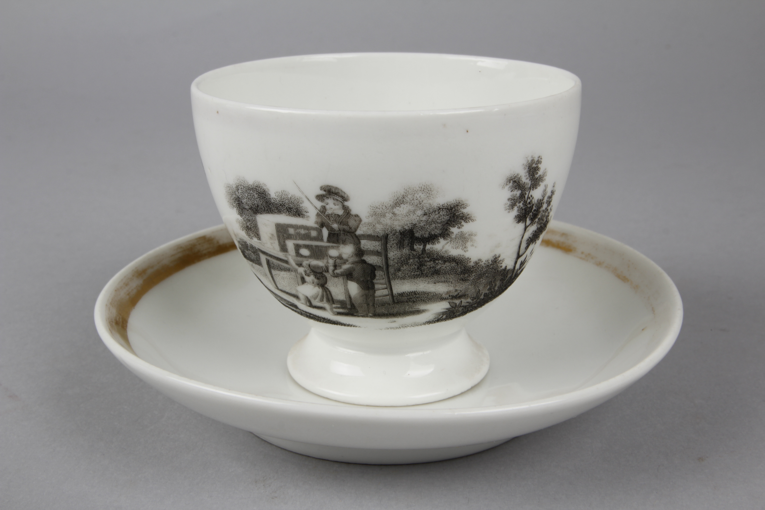 A White Bone China Cup and Saucer with a Lithographed Image of a Peepshow on the Side of the Cup,