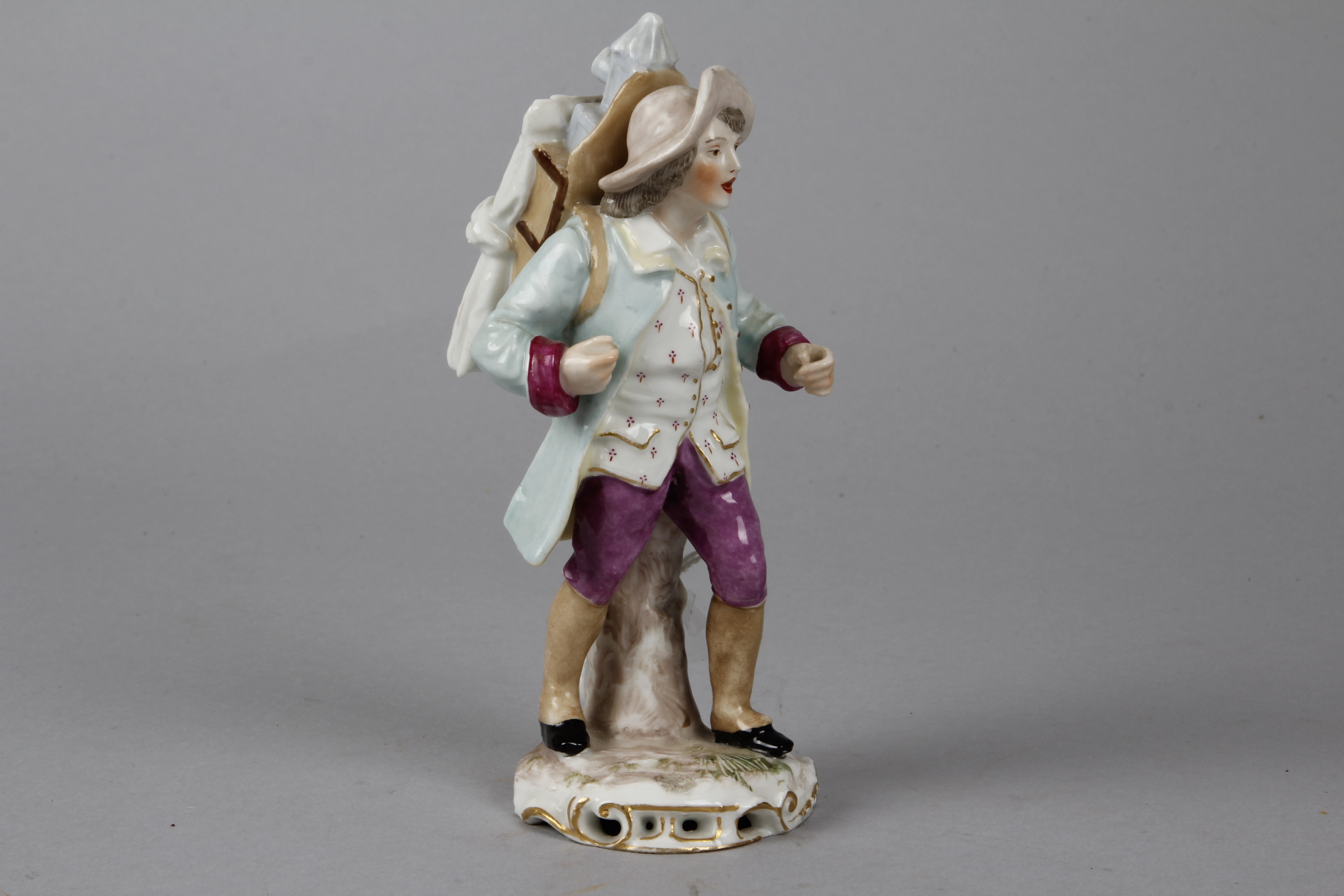 A Continental Porcelain Figurine of an Itinerant Magic Lanternist, the painted figure wearing a