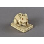 A Japanese ivory netsuke, modelled as an albino rabbit with red eyes seated upon a mono gotari