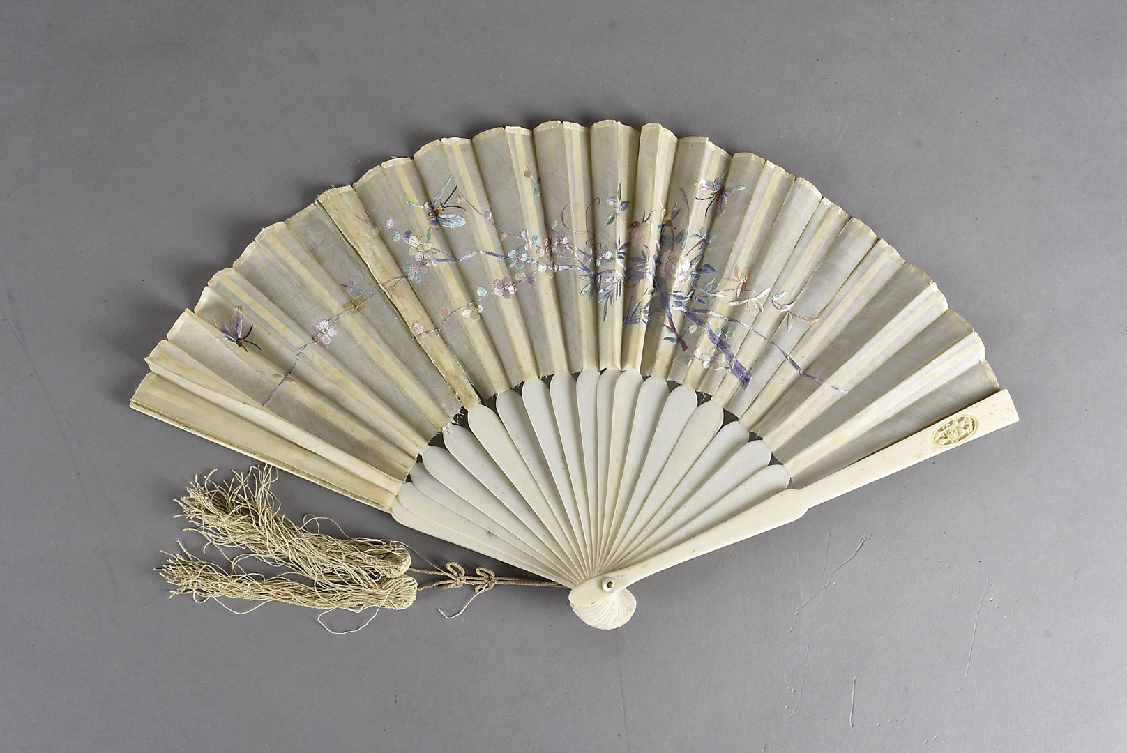 A Meiji period bone and embroidered silk fan, decorated with pink and mauve blossoms and three
