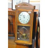 An oak wall clock with a silvered dial and visible