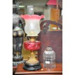 An oil lamp with cranberry glass shade