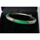 A vibrant green jade bangle held in a 925 silver bangle etched with light detailing in a