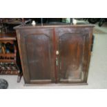 An oak hanging cabinet with a pair of double doors enclosing a single shelf