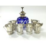 Six silver miniature three handled wine cups and a blue cut glass silver lidded perfume bottle.