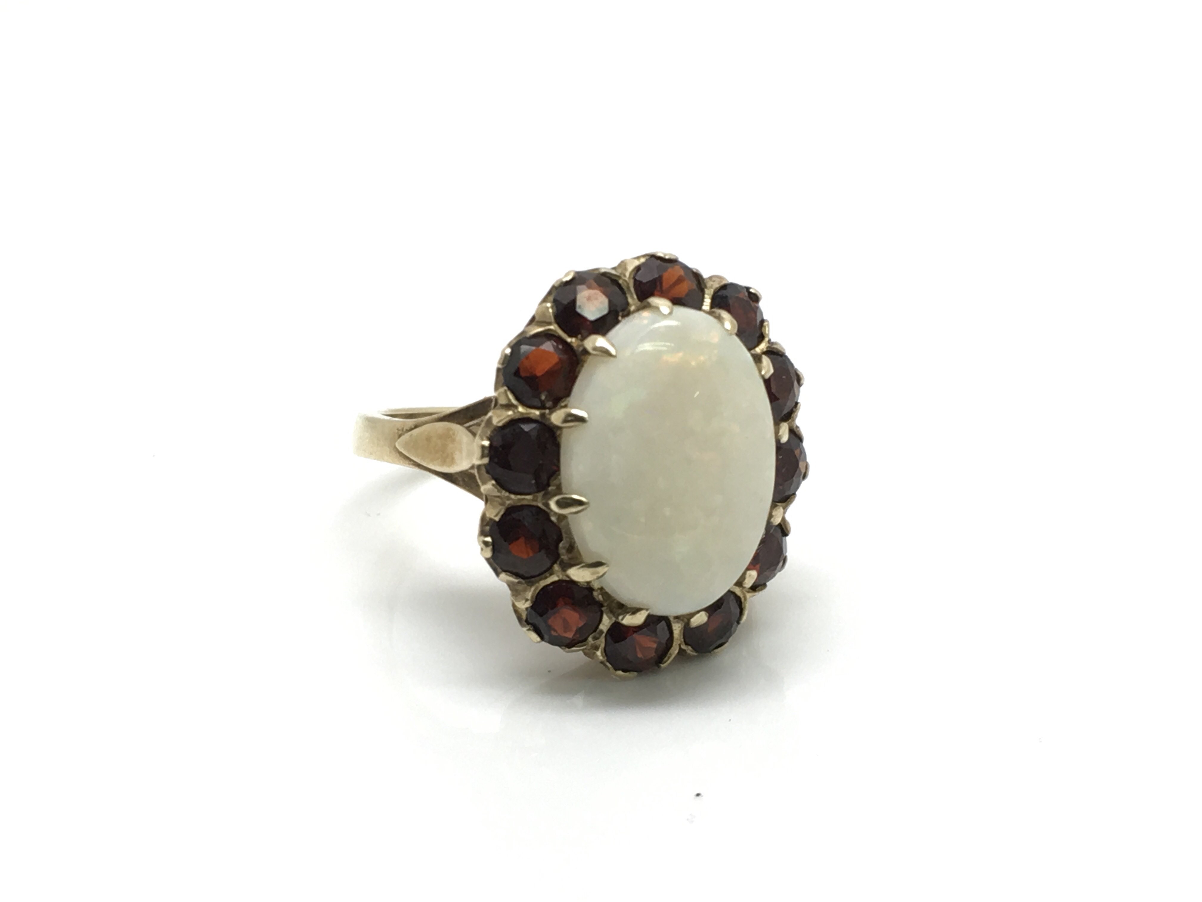 A ladies 9ct gold ring inset with a large central opal surrounded by 12 garnet rubies, ring size