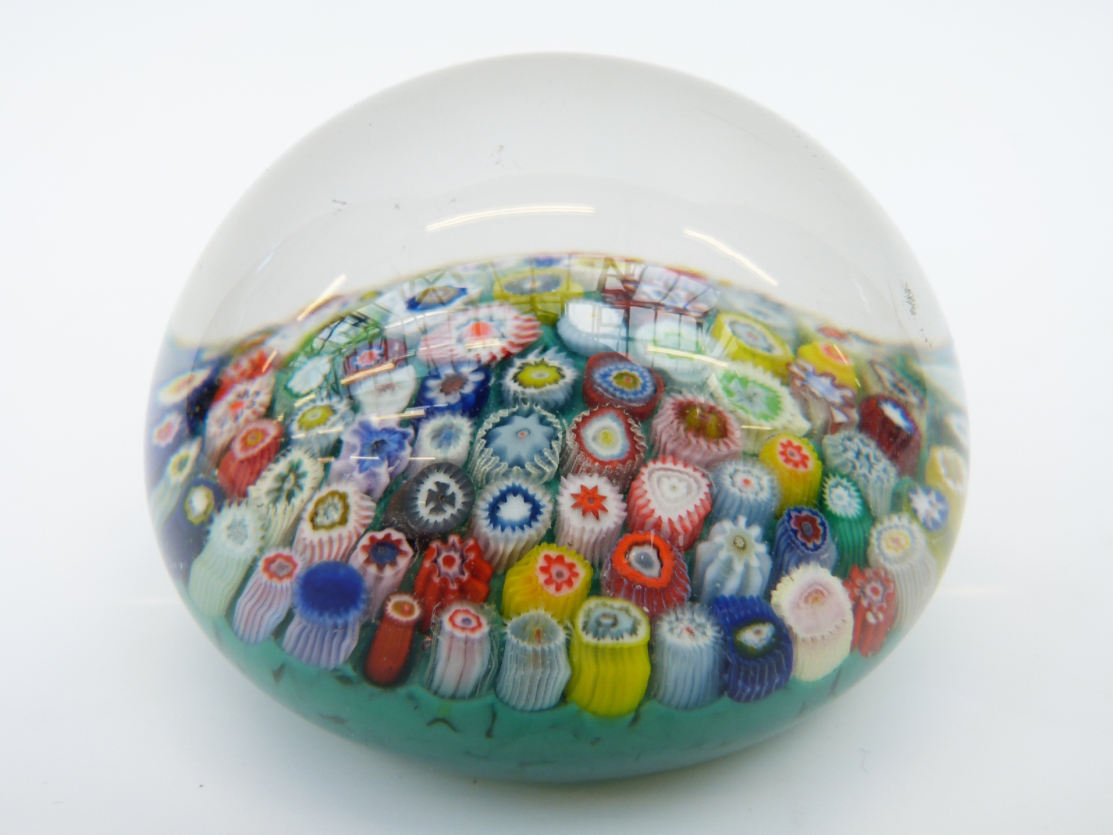 A millefiori glass paperweight with various multicoloured canes on a turquoise ground,