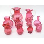 Ten cranberry glass jugs, some with etched decoration, all with applied clear handles,