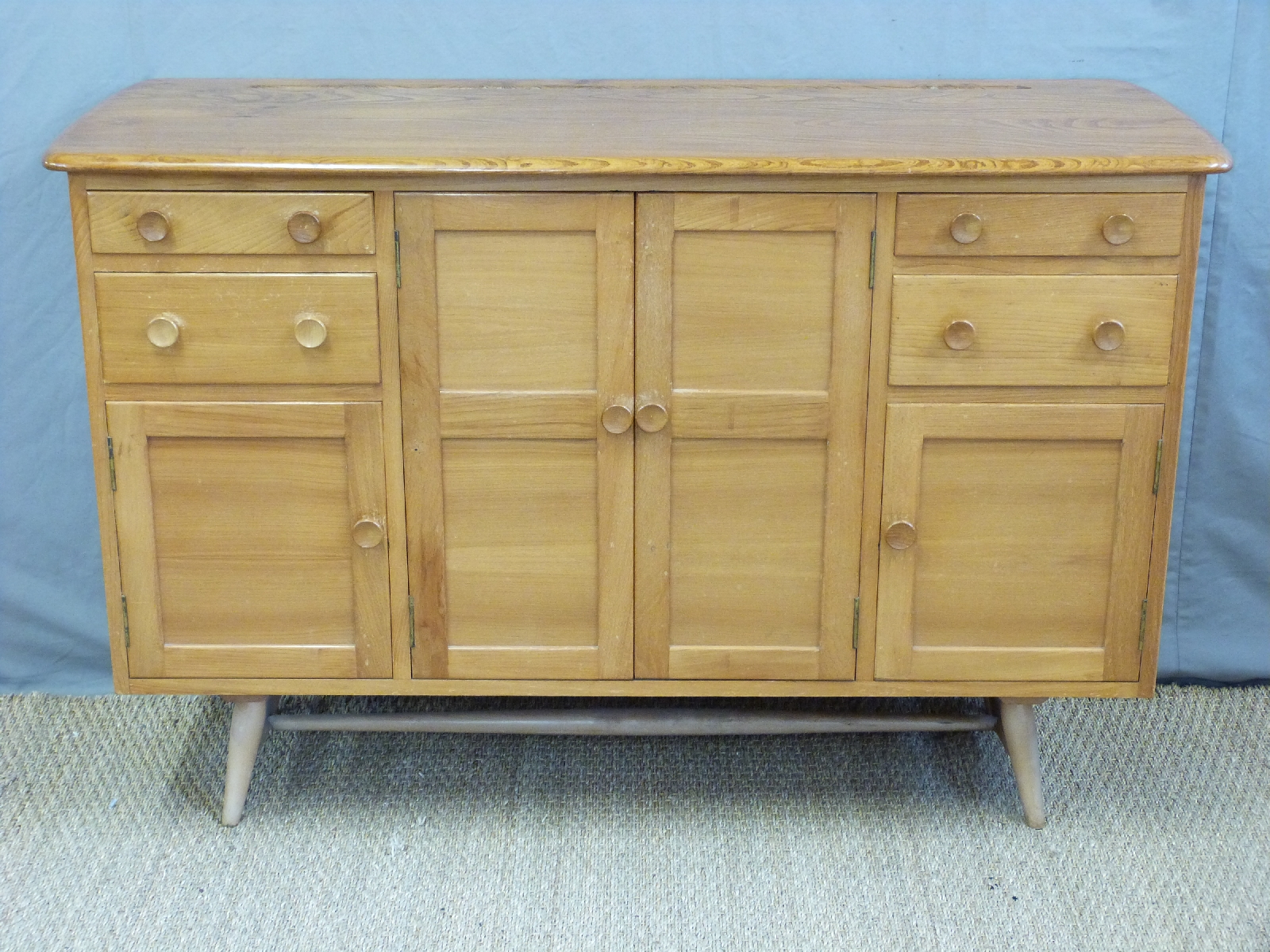A retro Ercol light elm sideboard with an arrangement of four cupboard doors and four drawers inc