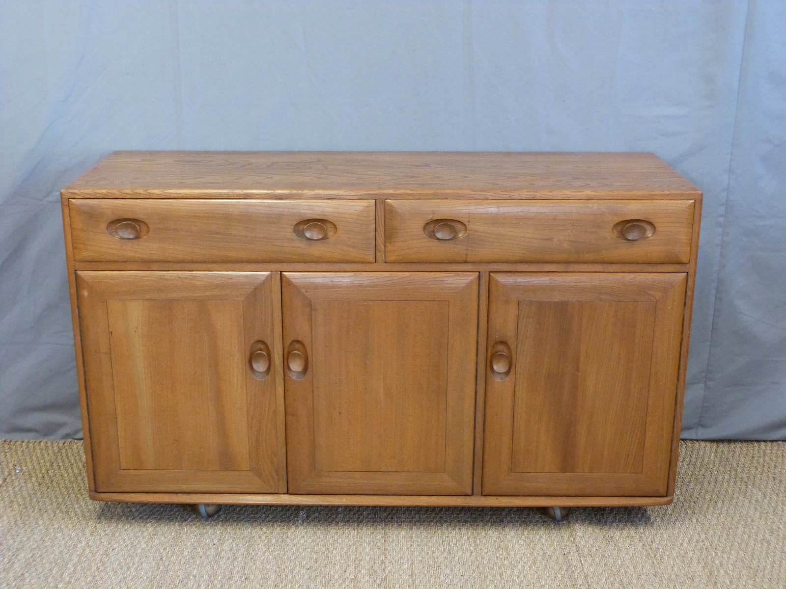 A retro Ercol light elm sideboard with an arrangement of two drawers over three doors (H81 x W106 x