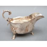A George V hallmarked silver sauce or gravy boat with scroll handle raised on three feet,