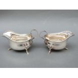 A pair of George V hallmarked silver gravy or sauce boats, raised on three feet with scroll handle,
