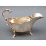 A Edward VII hallmarked silver sauce or gravy boat with scroll handle raised on three feet,