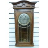 An oak-cased c1910 wall clock in lightly carved case with, bevelled glass door,