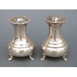 A pair of George V hallmarked silver peppers raised on three feet, Sheffield 1919 and 1926,