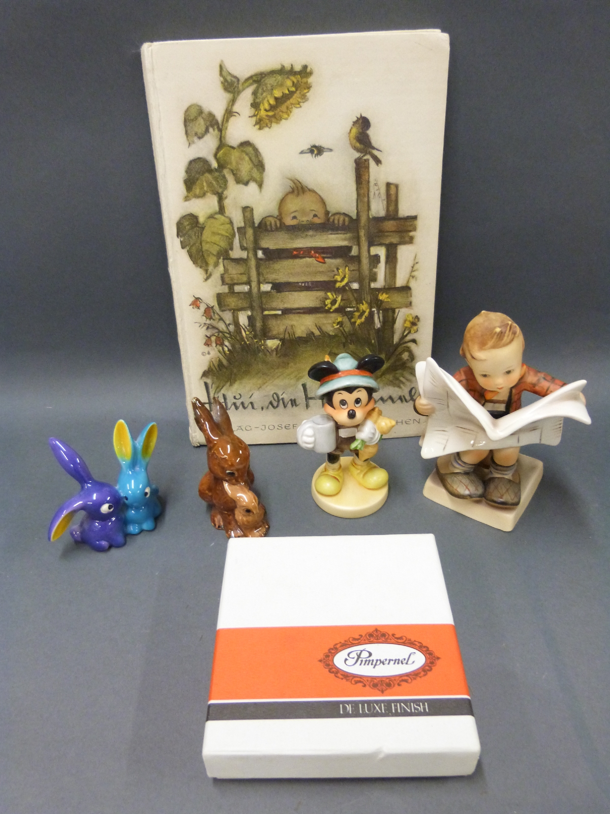 Four Goebel Hummel figures including boy reading newspaper, Mickey Mouse and unusual rabbits,