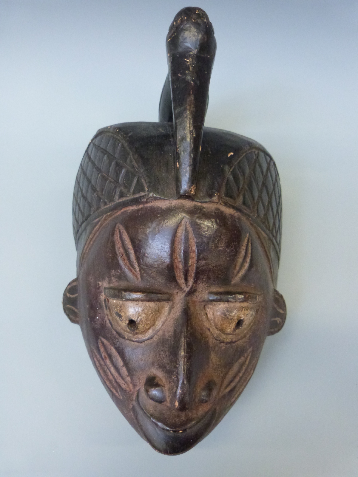 A tribal carved wooden mask decorated with a bird