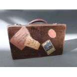 A tan leather mock crocodile suitcase with vintage travel labels, approximately 40cm long.