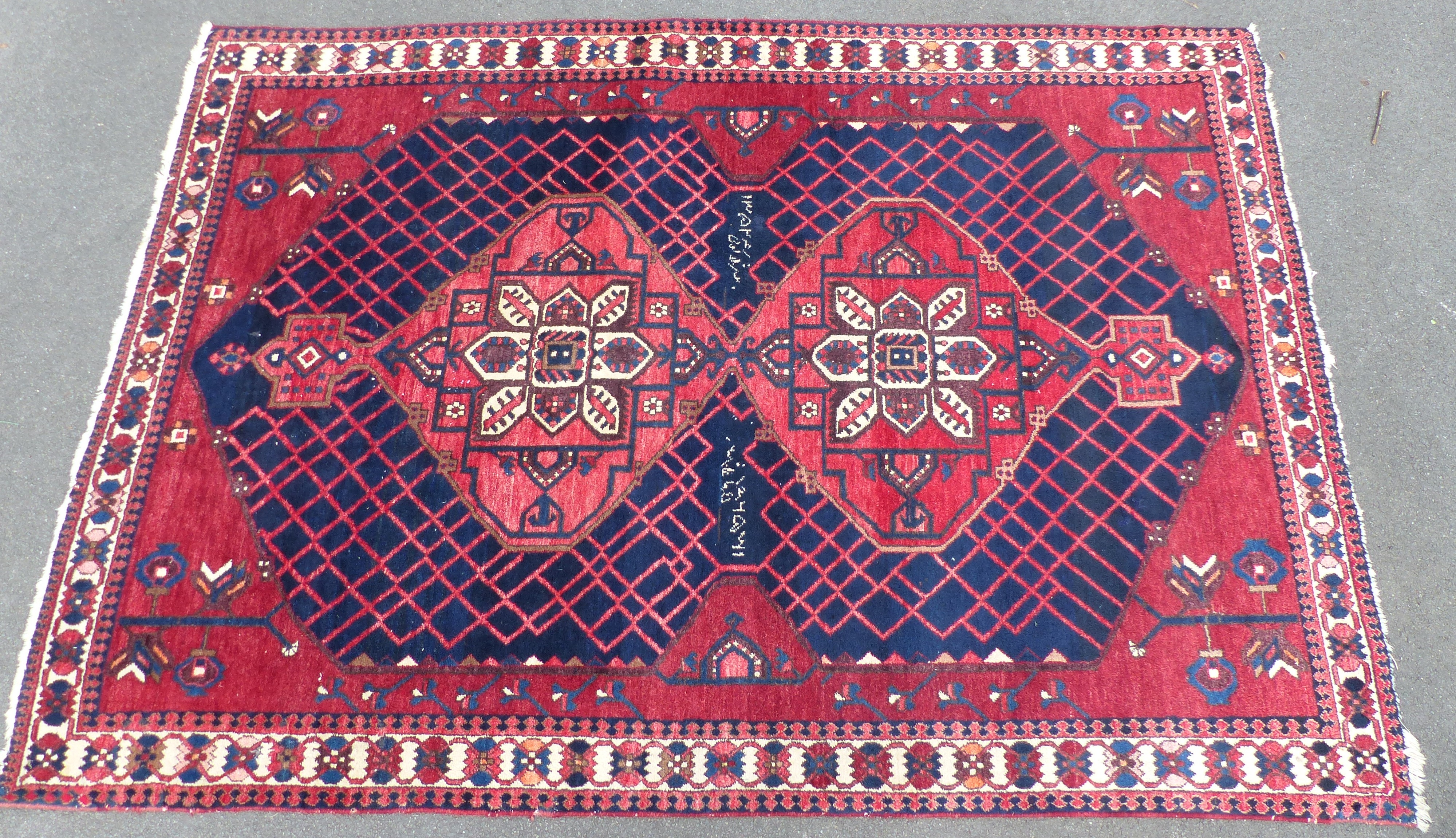 A Persian Shzad hand made red ground rug with stylised flowers to corners and Islamic script to