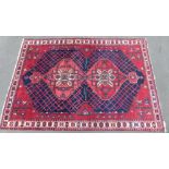 A Persian Shzad hand made red ground rug with stylised flowers to corners and Islamic script to