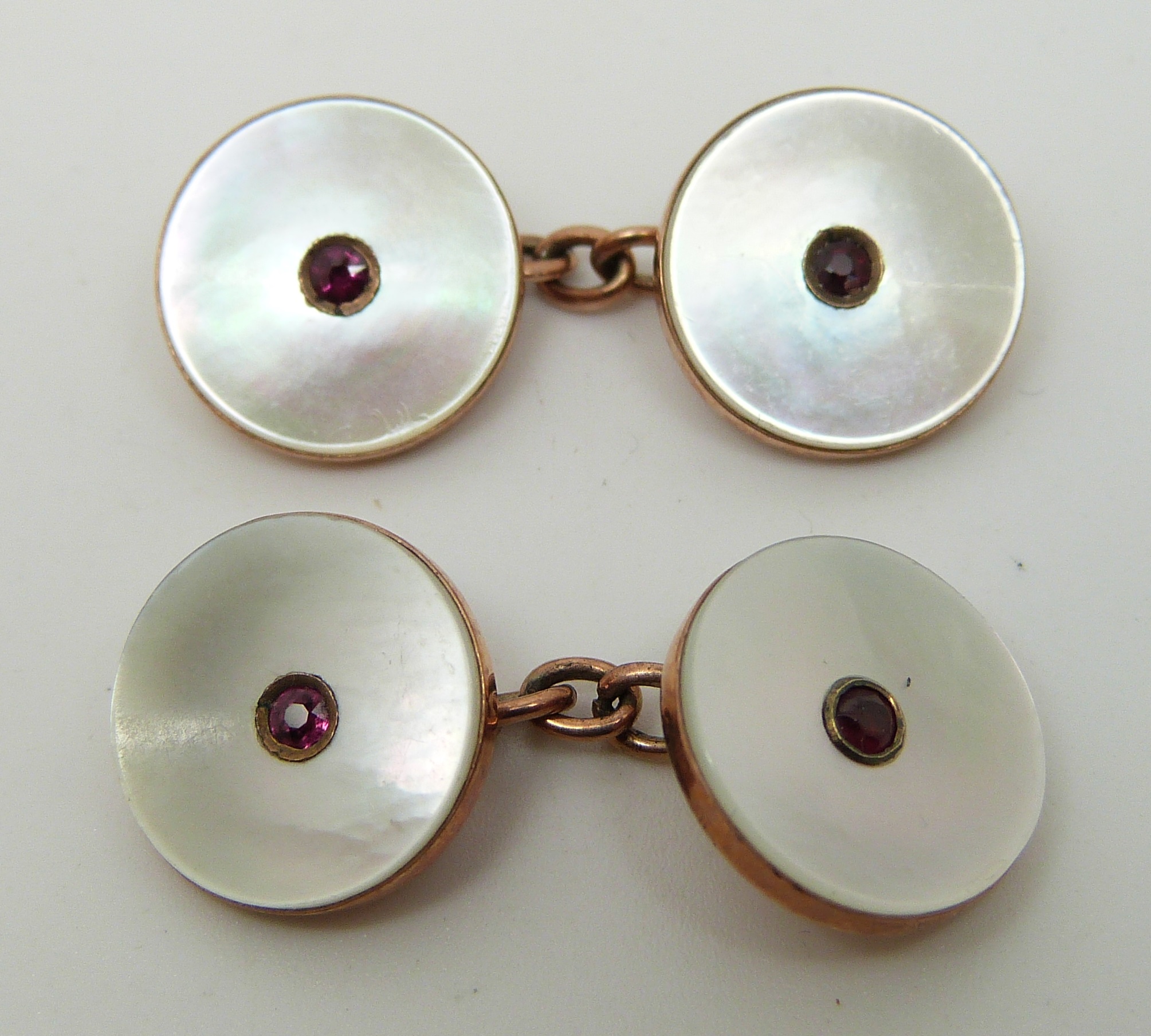 A pair of rose gold cufflinks set with pink paste to the centre and mother of pearl