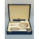 A cased hallmarked silver three piece dressing table set comprising mirror and two brushes,