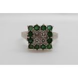 An 18ct gold white gold ring set with four diamonds surrounded by emeralds in a square setting