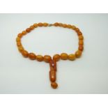 An amber prayer bead necklace of 28 graduated ovoid egg yolk coloured beads and two larger barrel