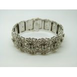 A white metal bracelet with raised floral decoration and each panel set with three cubic zirconia