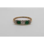 An 18ct gold ring set with three round cut diamonds and two square cut emeralds (size O)