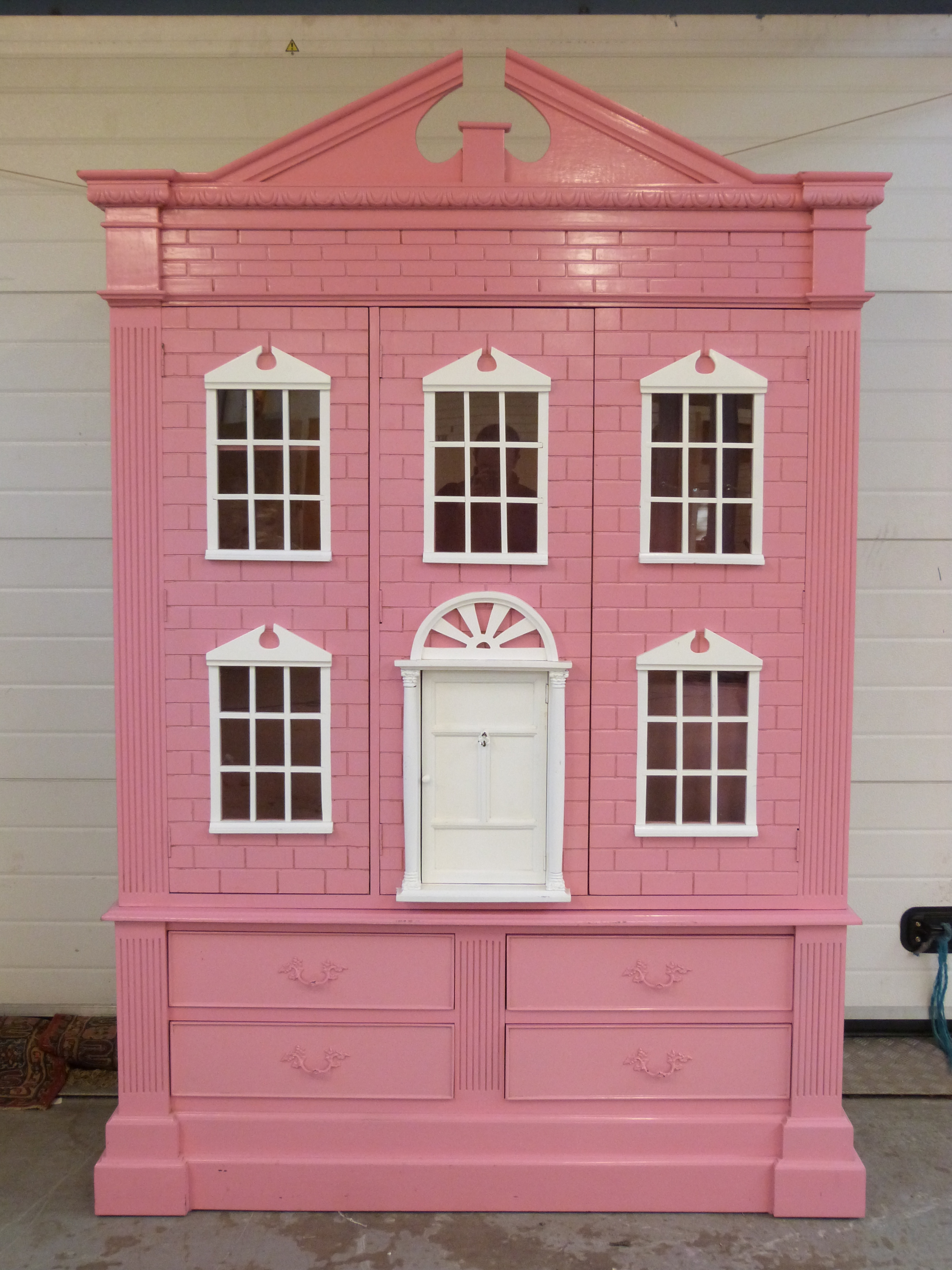 A pink painted child's wardrobe in the form of a doll's house,