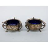 A pair of Edward VII hallmarked silver open salts with blue glass liners, on raised hoofed feet,