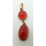 A yellow metal pendant set with a circular red cabochon and an oval red cabochon