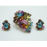 A silver brooch set with coloured paste in a stylised floral decoration and matching earrings