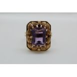 An 18ct gold ring set with an emerald cut amethyst with foliate border, 6.