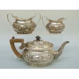 An Edward VII hallmarked silver three piece tea set with repoussé decoration and vacant cartouches,