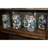 A large collection of coloured glass marbles, contained within seven clear glass storage jars.