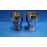 A pair of metal beakers, engraved 'Compliments M.G Shahani & Co', 10.5cm.