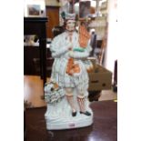 A Victorian Staffordshire highland pottery figure of a man with bagpipes and dog, 41.5cm high.