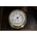 A brass bulkhead style aneroid barometer, on stained pitch pine mount, the whole 26.5cm diameter.