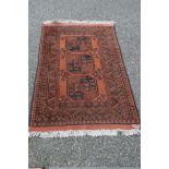 An Afghan rug, with three gul motifs on a rusty red field, 135 x 81cm.