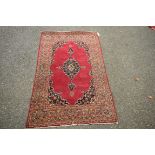 A Persian Kashan rug, with a central floral medallion on a plain red field,