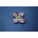 A silver and lilac enamel flower form brooch, set with central peridot surrounded by pearls.