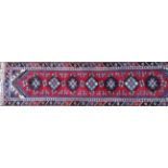 A PERSIAN RUNNER CARPET/RUG With a single row of hooked lozenge form motifs contained within a red