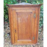 A 19TH CENTURY OAK WALL HANGING CORNER CUPBOARD With a dentil frieze above a single panelled door,